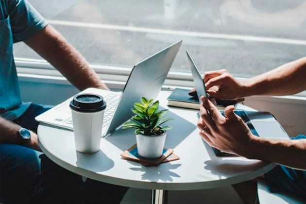 Two people with laptops on a small white coffee table. Two people with laptops on a small white coffee table.